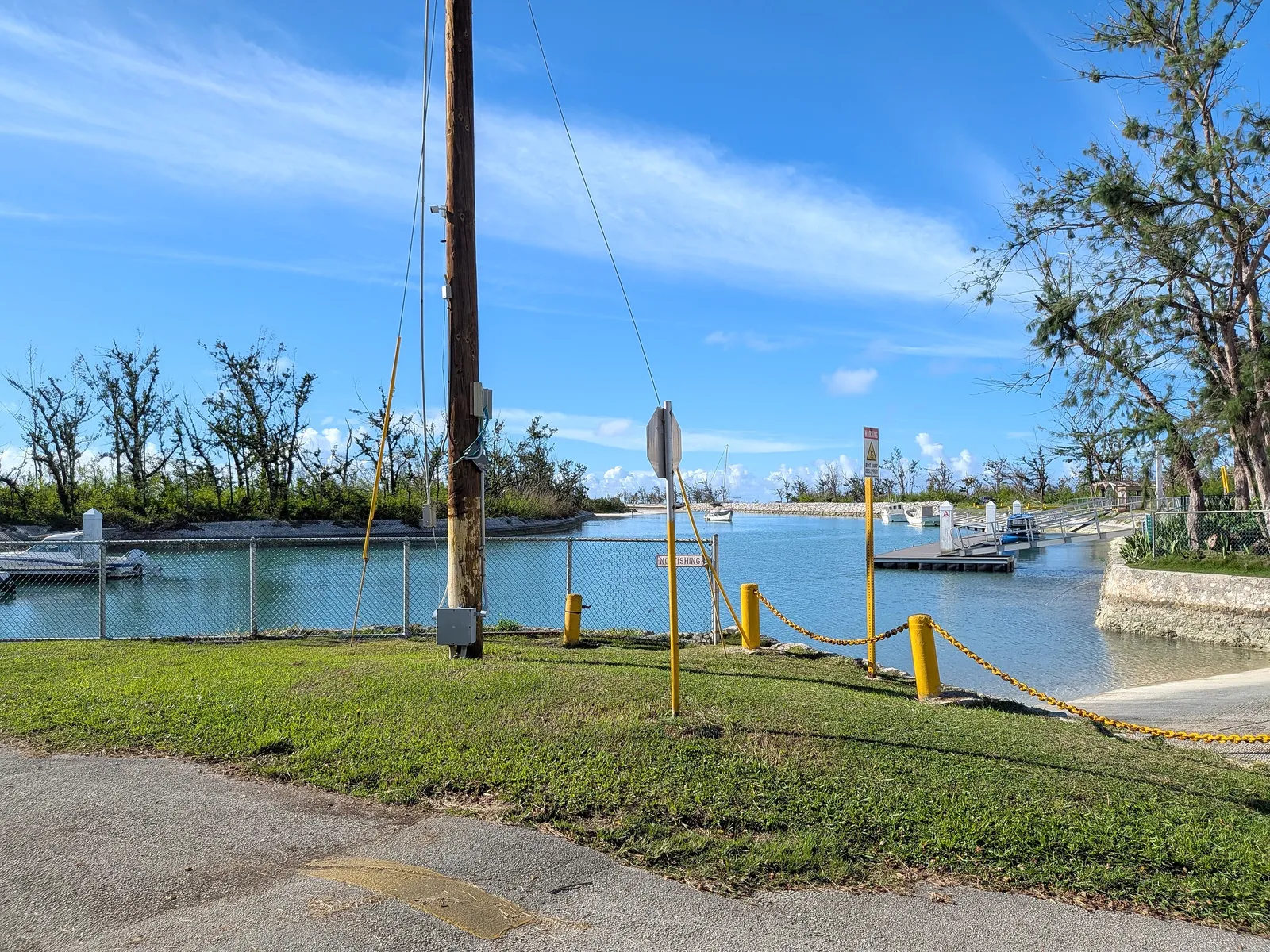 The boat channel and launch ramp at Smiling Cove Marina, with a posted no-fishing sign and a sailboat moored beyond