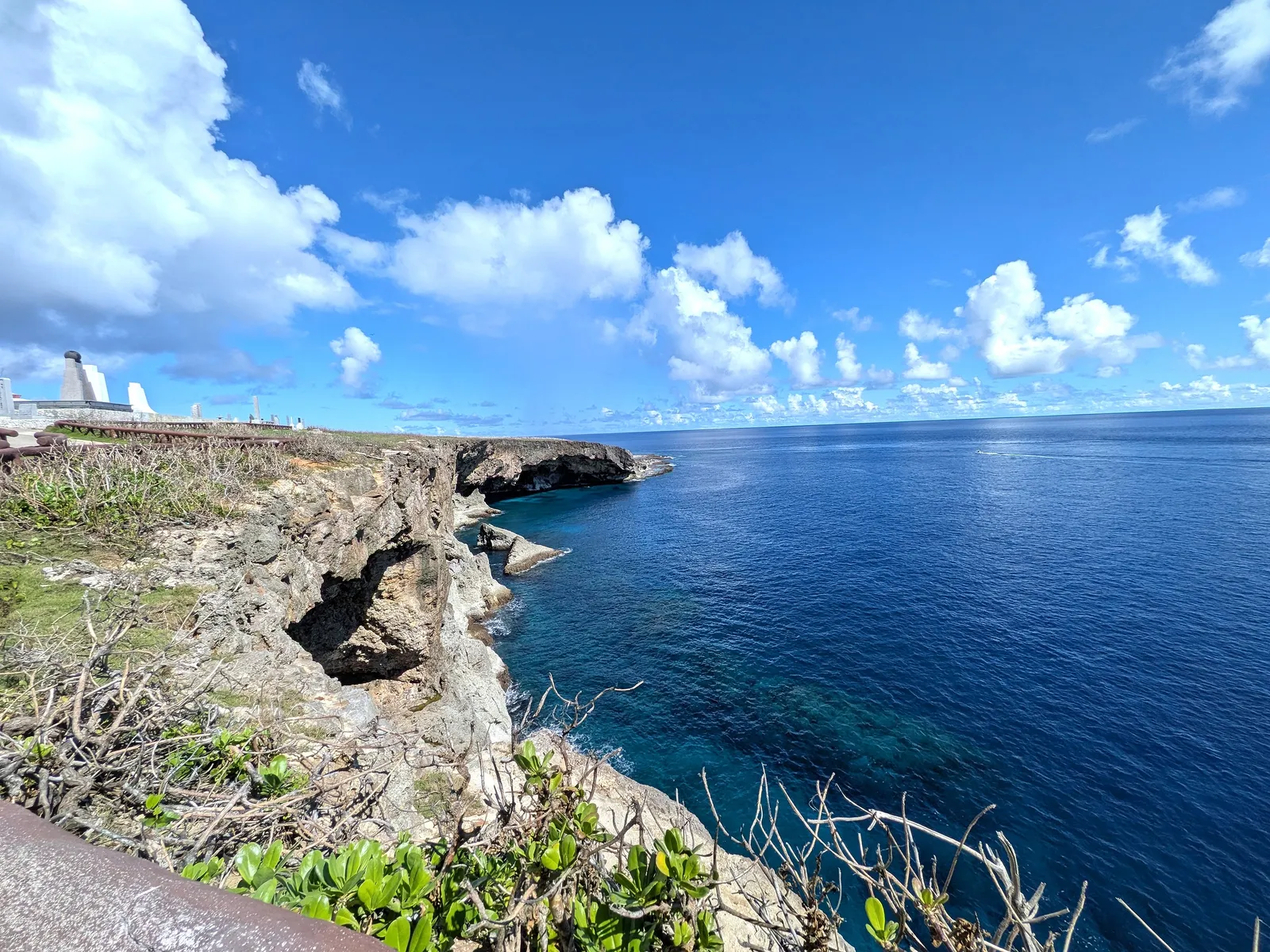 The limestone cliff face below Banzai Cliff, dropping into deep blue water, with the memorial park visible along the headland above