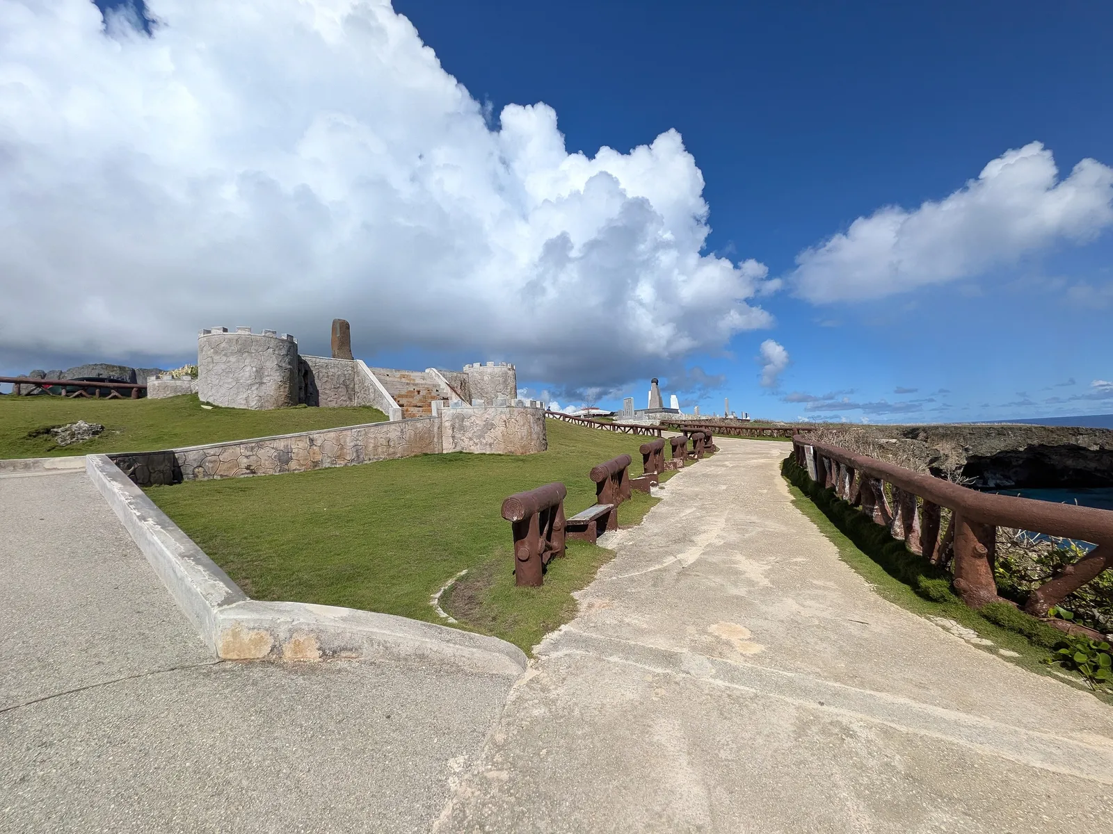 The paved walkway at Banzai Cliff leading toward the monuments, with a railed drop to the sea on the right