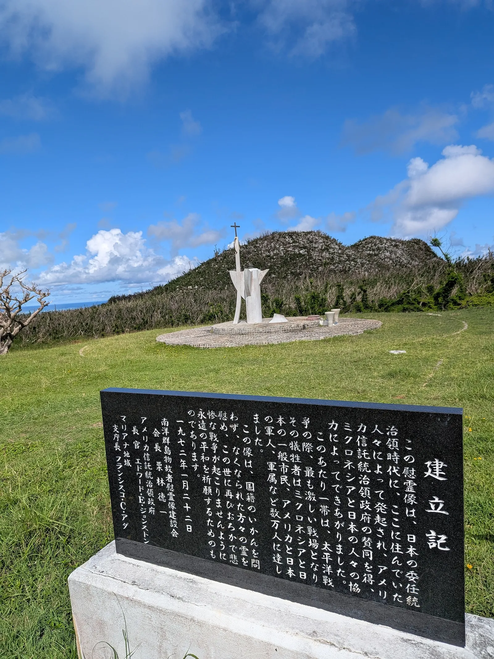 The black granite founding stone at Suicide Cliff, inscribed in Japanese and dated January 22, 1972, with the peace statue visible behind it