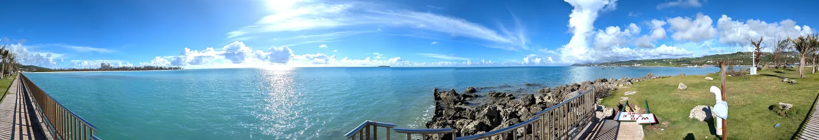 Panorama from the seawall at Smiling Cove Marina, sweeping from the Garapan shoreline across the lagoon to the rocky point