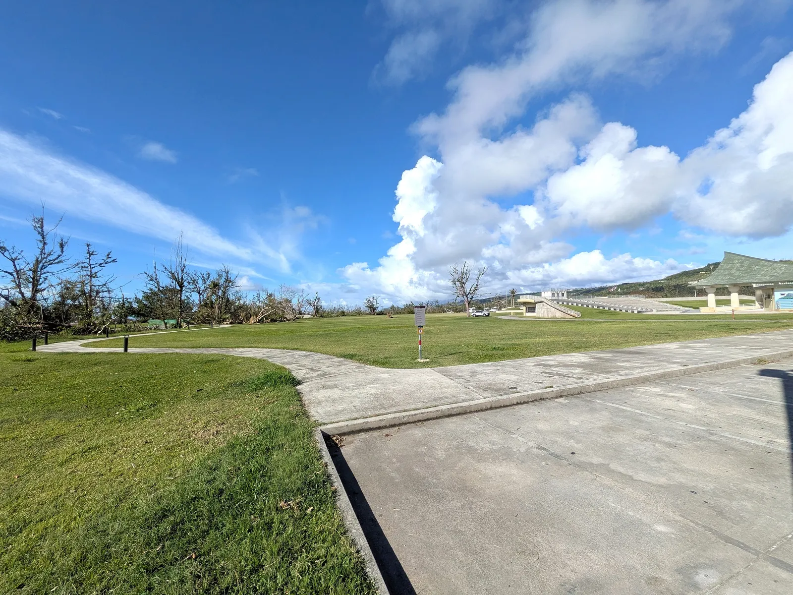Open lawn and a curving footpath at American Memorial Park, with the amphitheater visible in the distance