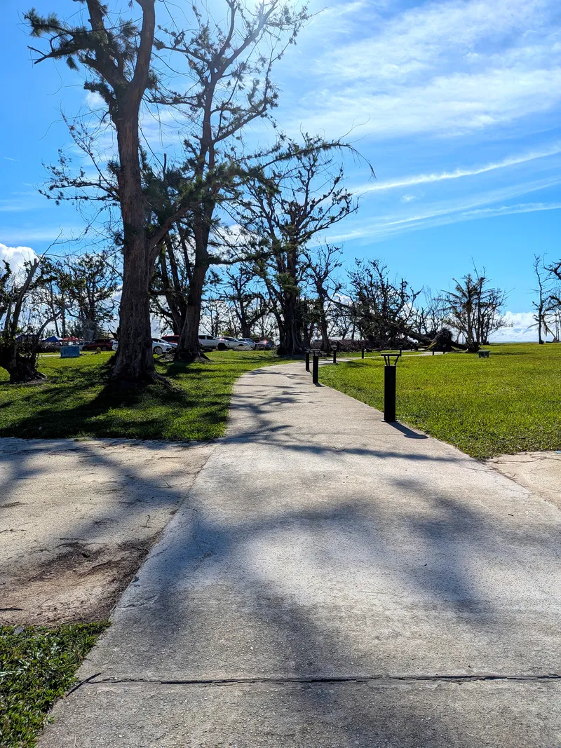 Paved walking and jogging path along Micro Beach with parked cars and beach umbrellas set up by locals